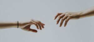 Two hands reaching to touch each other on a grey background.